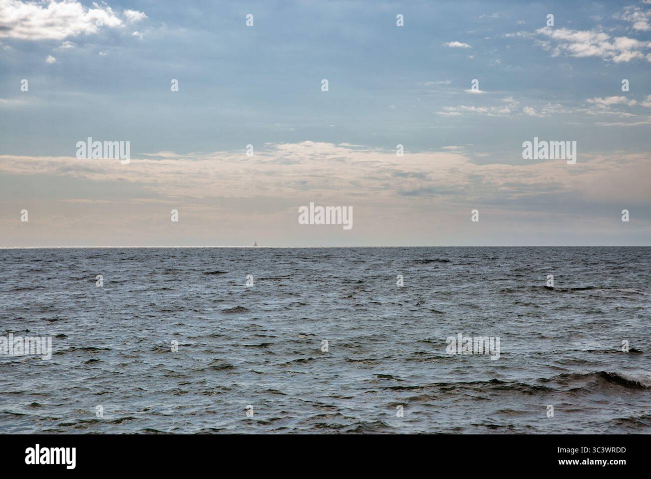 Sereno paesaggio marino con onde dolci sulla superficie dell'acqua scura che si estende fino all'orizzonte lontano sotto un cielo blu parzialmente nuvoloso con nuvole bianche e soffici. Foto Stock
