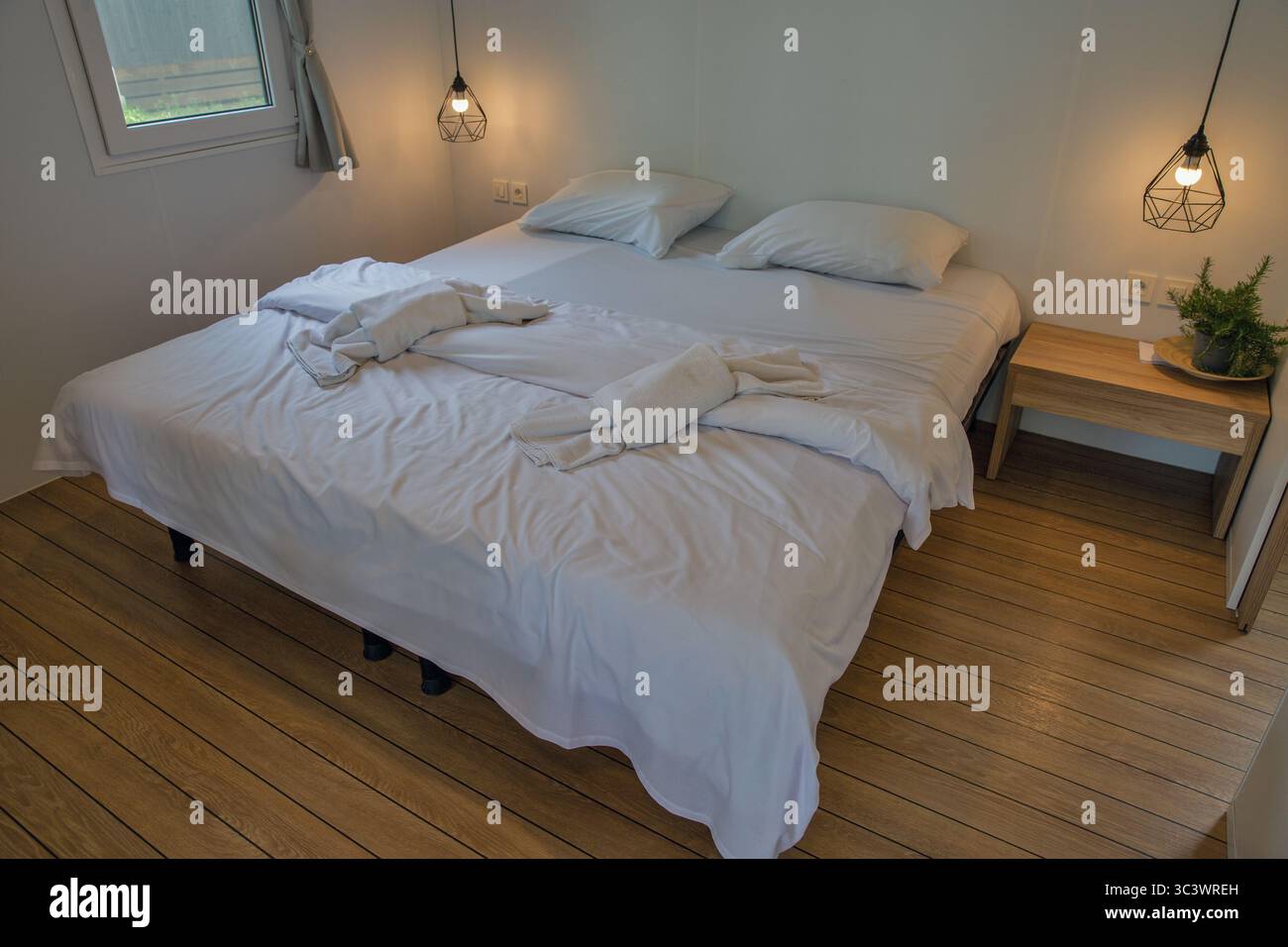 Lenzuola bianche pulite sul letto a piattaforma con caldi pavimenti in legno, lampade a sospensione geometriche a filo e luce naturale dalla finestra. i scandinavo contemporaneo Foto Stock