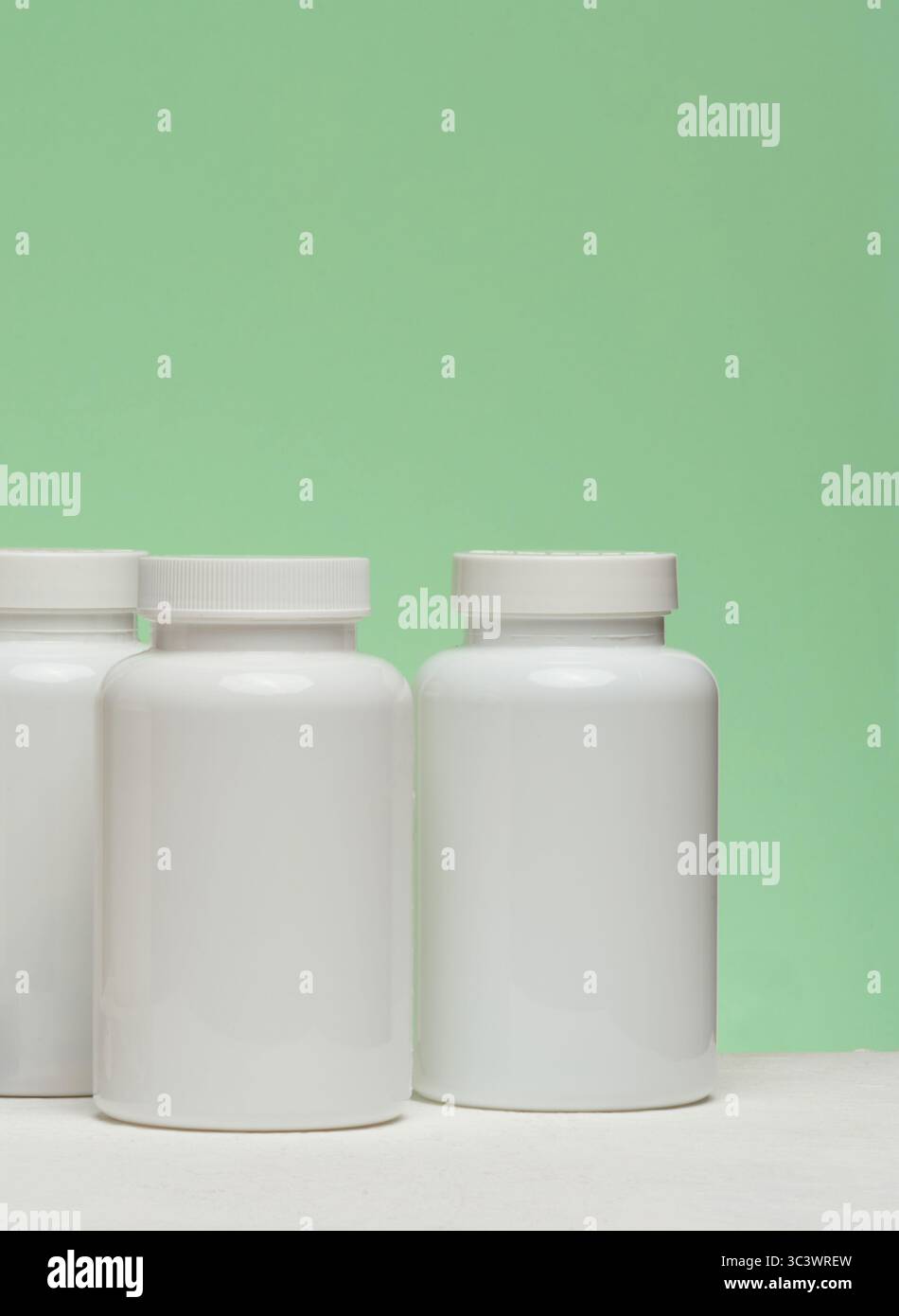 Diversi vasetti di plastica bianchi con pillole su sfondo verde. Articoli relativi alla medicina e all'assistenza sanitaria Foto Stock