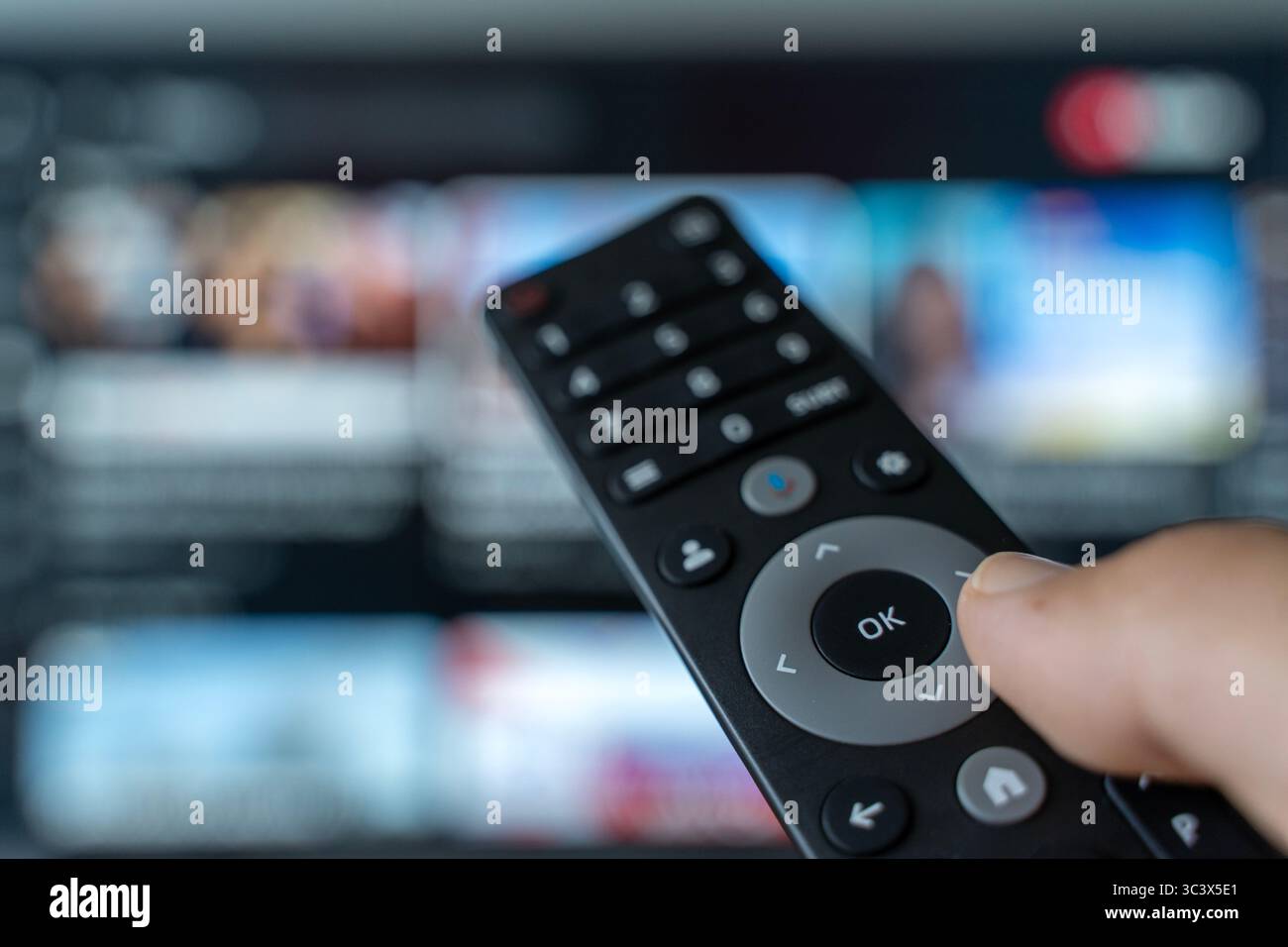 Una mano che tiene in mano il telecomando commuta i canali di un televisore con uno schermo sfocato sullo sfondo. Le riprese simboleggiano il moderno consumo dei media, il sovraccarico di contenuti, l'affaticamento delle scelte digitali e la costante ricerca di informazioni coinvolgenti. Ideale per temi riguardanti le abitudini multimediali, l'intrattenimento, l'età dell'informazione e la dipendenza dallo schermo. Foto Stock