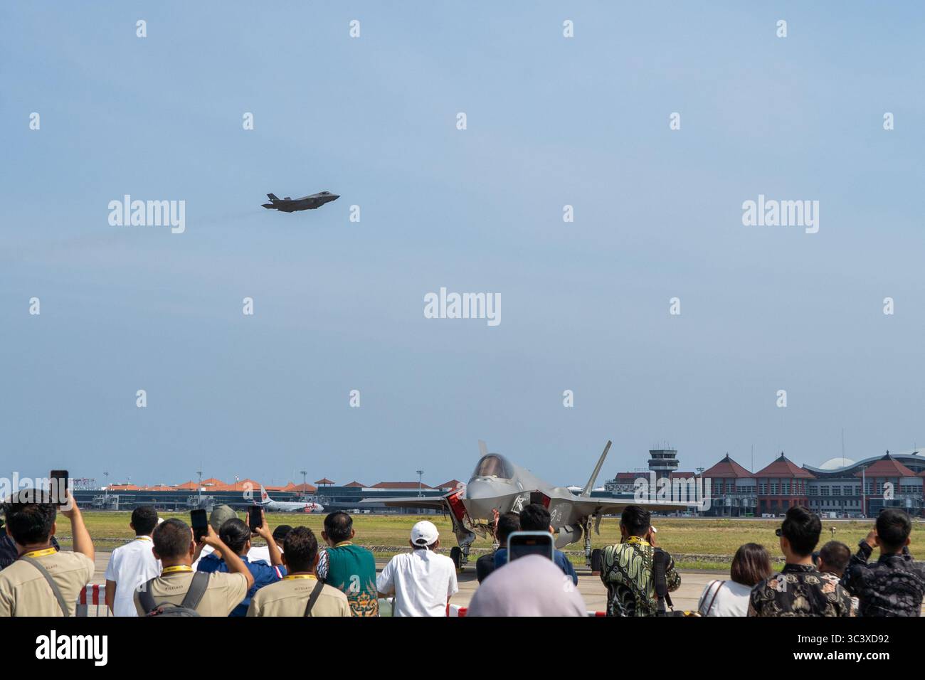 Bali, 18 settembre 2024: I combattenti furtivi ruggiscono sopra la testa mentre la folla fotografa getti sull'asfalto sotto il cielo limpido. Foto Stock