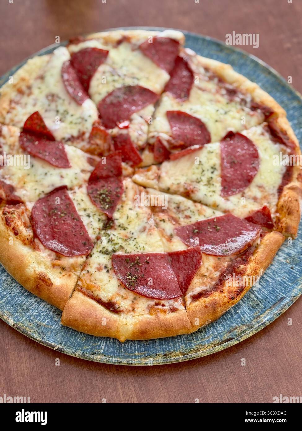 Primo piano di una pizza al peperoni con formaggio fuso su un piatto di legno rustico, Lübeck, Germania. Foto Stock