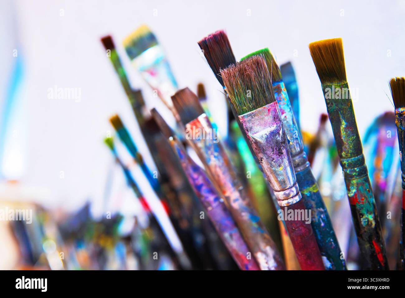 Un gruppo di pennelli ben usati con vernice colorata asciutta sui manici e setole in contenitore nello studio d'arte creativo. Foto Stock