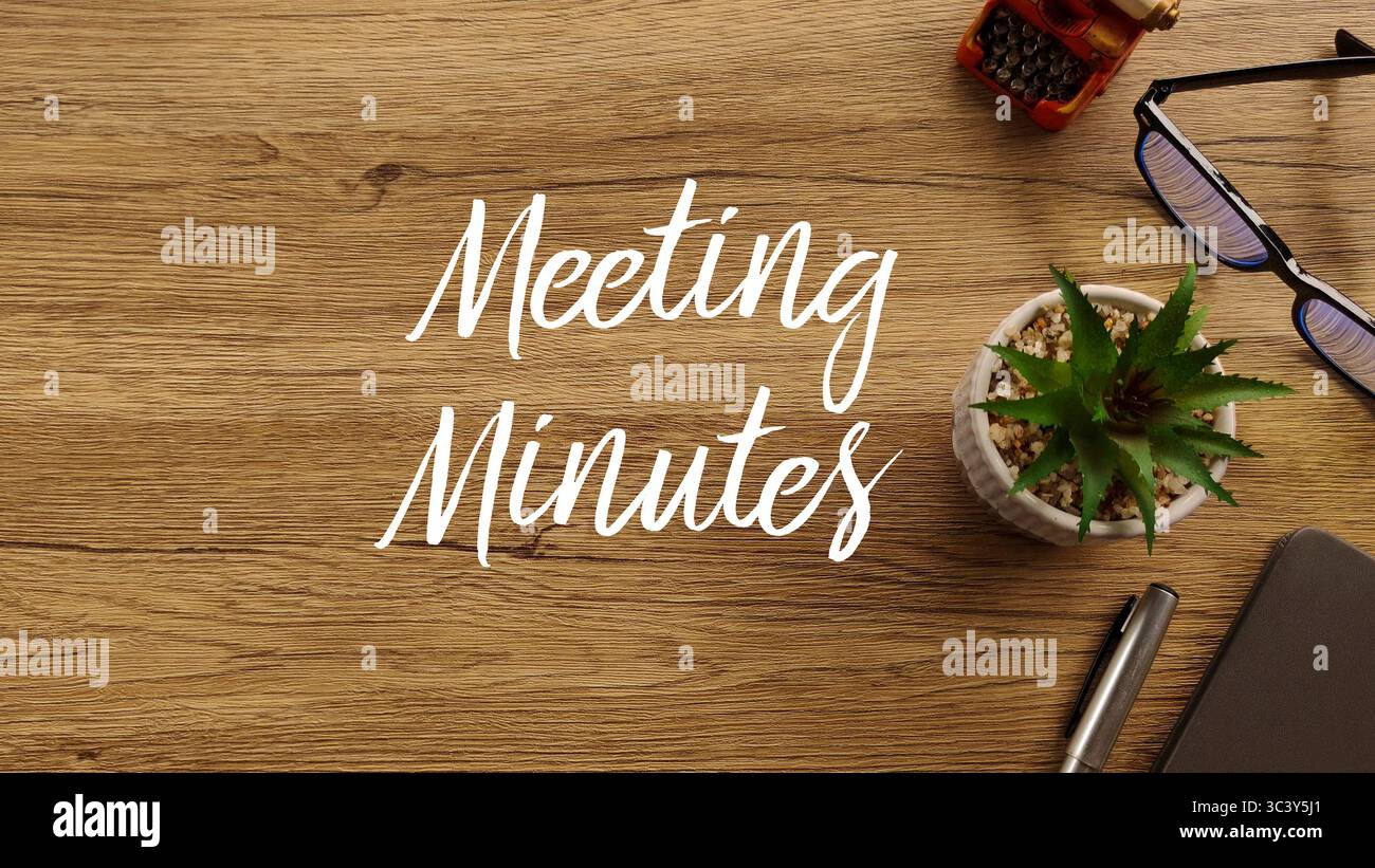 Vista dall'alto verso il basso di una scrivania in legno con testo "Meeting Minutes", circondata da piante succulente, penna, taccuino, macchina da scrivere vintage e bicchieri, con copia Foto Stock
