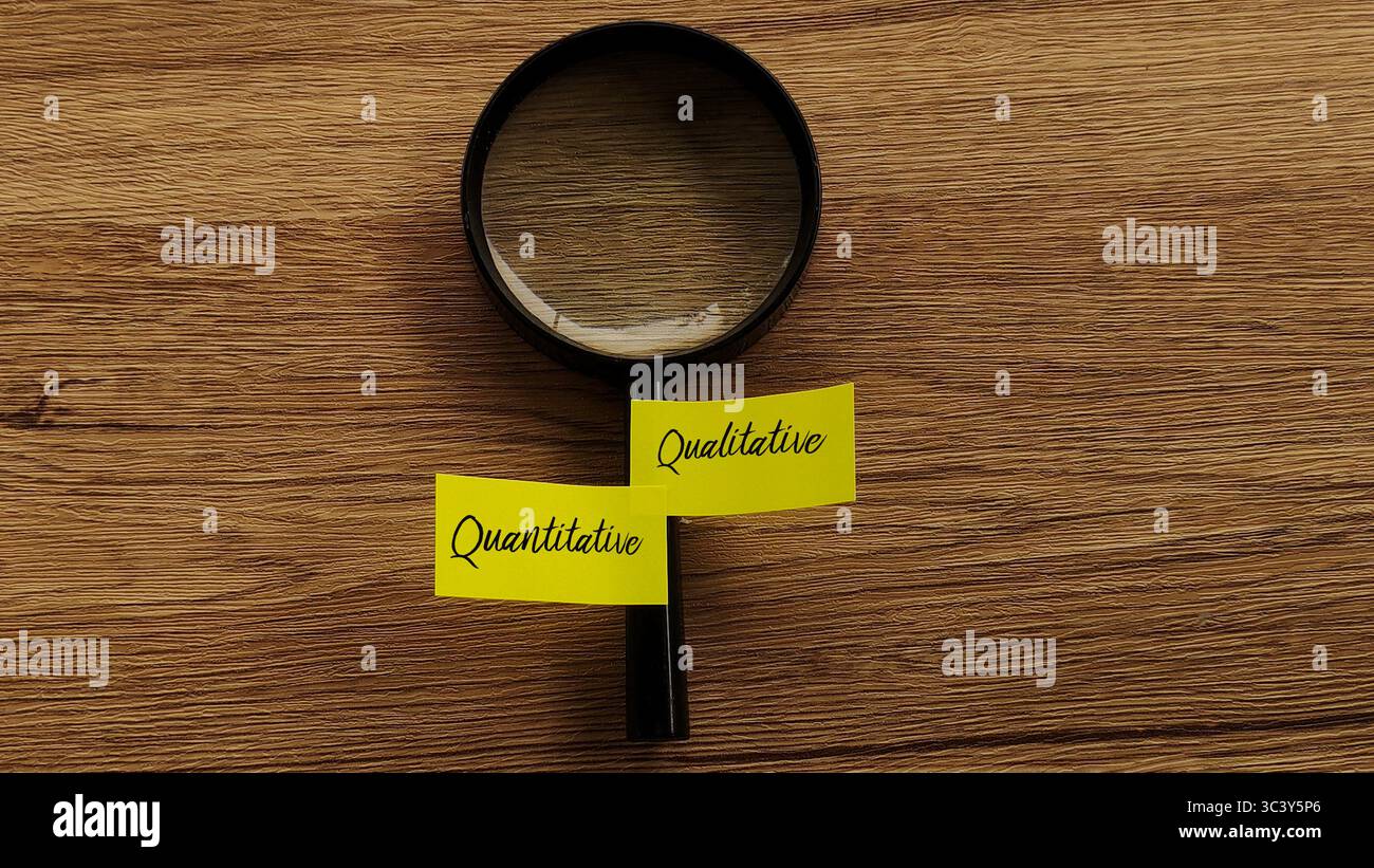 Vista dall'alto verso il basso di una lente d'ingrandimento su una scrivania in legno con due note adesive, una etichettata "quantitativa" e l'altra "qualitativa". Foto Stock