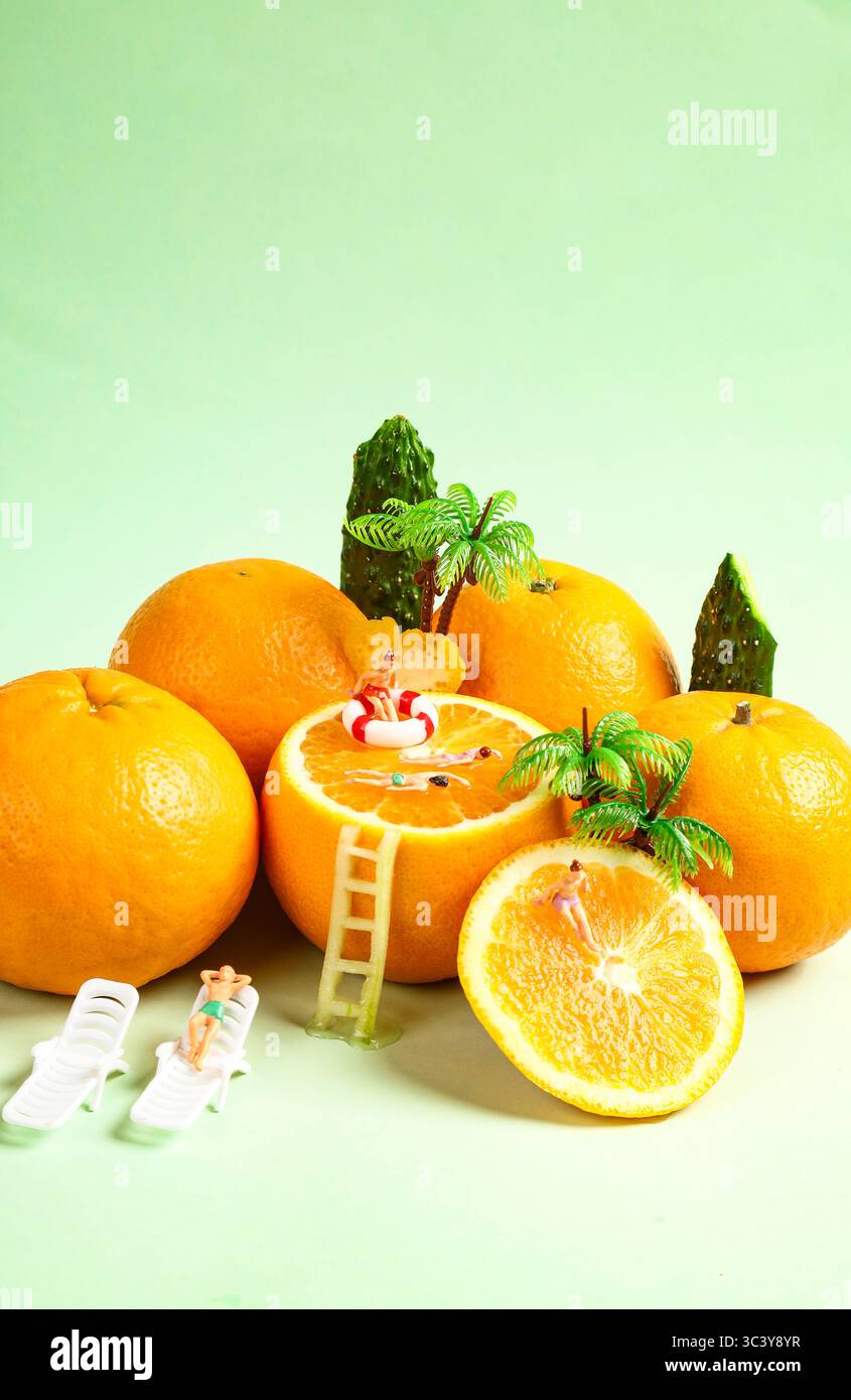 Persone in miniatura che si rilassano in un Tropical Orange Pool Paradise, arance con decorazioni natalizie su sfondo verde, concetto di Natale e Capodanno Foto Stock