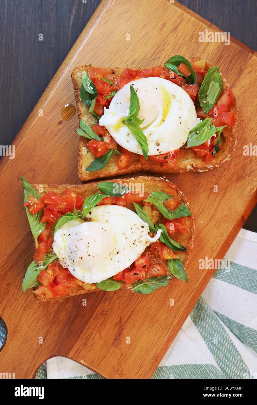 Un paio di uova appena cotte in camicia con toast al pomodoro fresco e basilico integrale Foto Stock