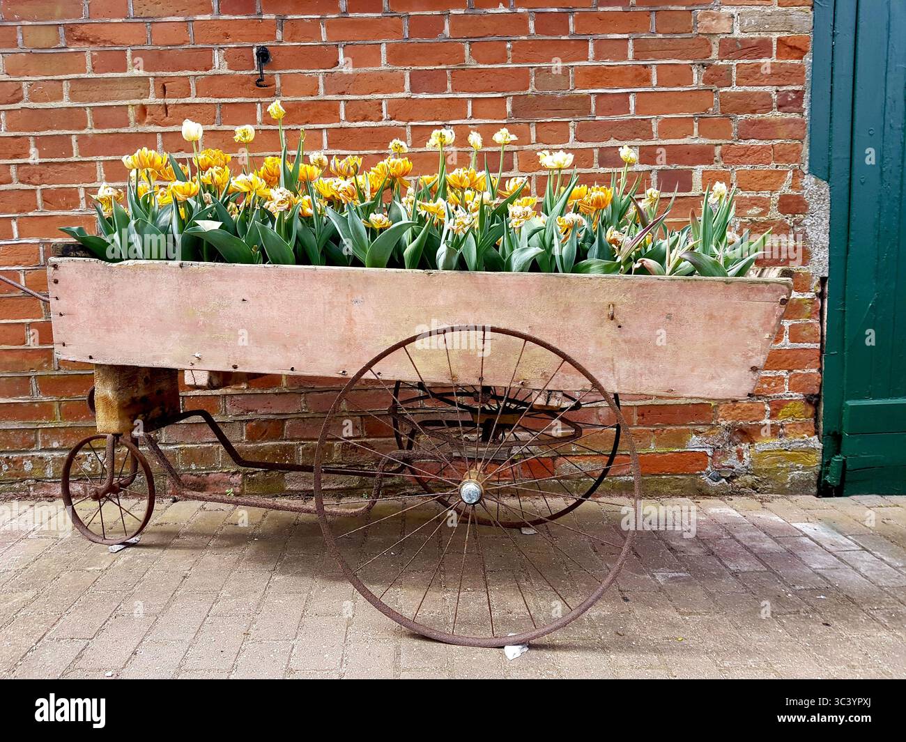 Un vecchio carro di legno con fiori esposti contro un vecchio muro di mattoni. Foto Stock