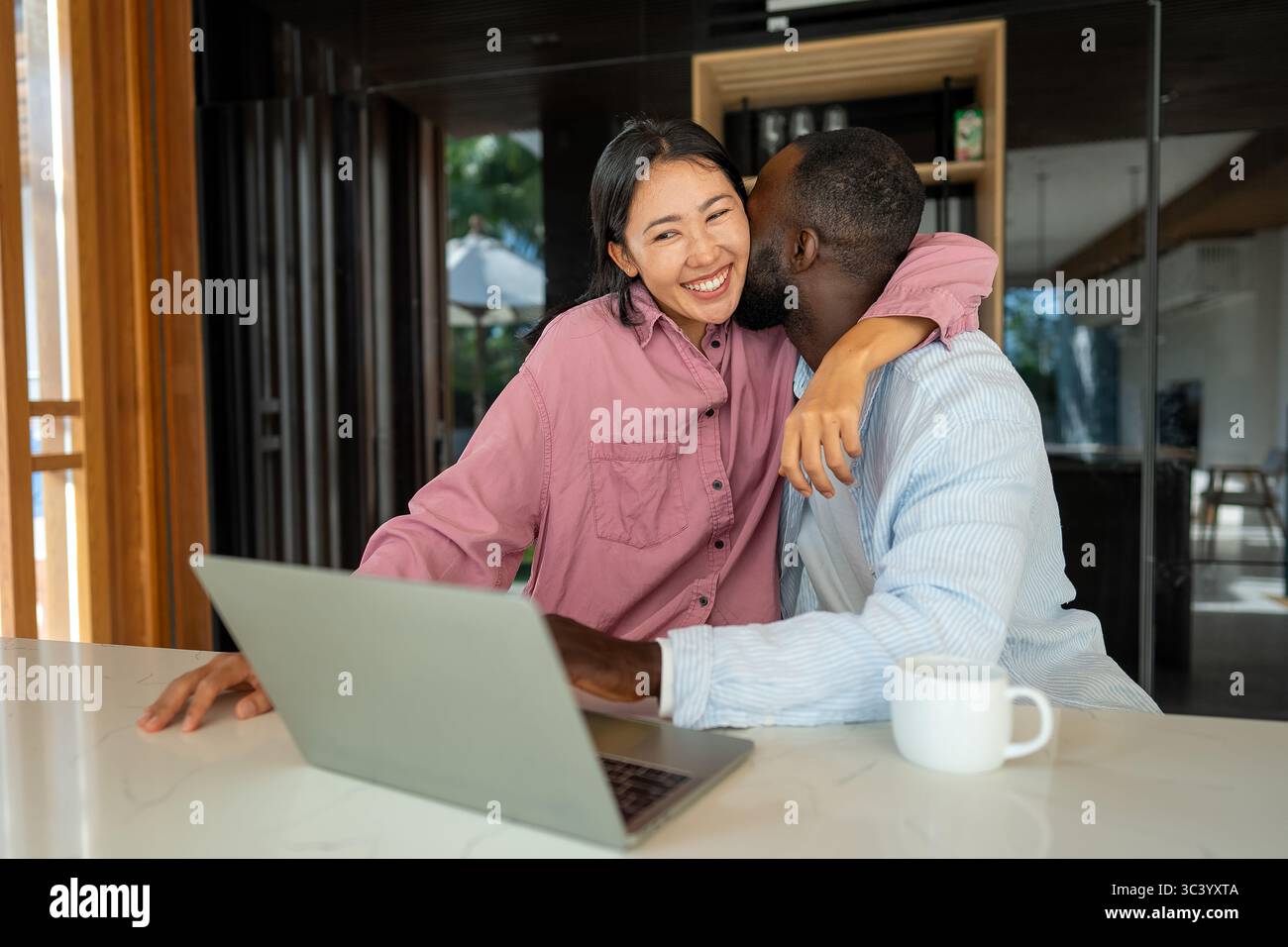 Felice coppia multietnica che utilizza un notebook, acquista online con le vendite, gioca insieme Foto Stock