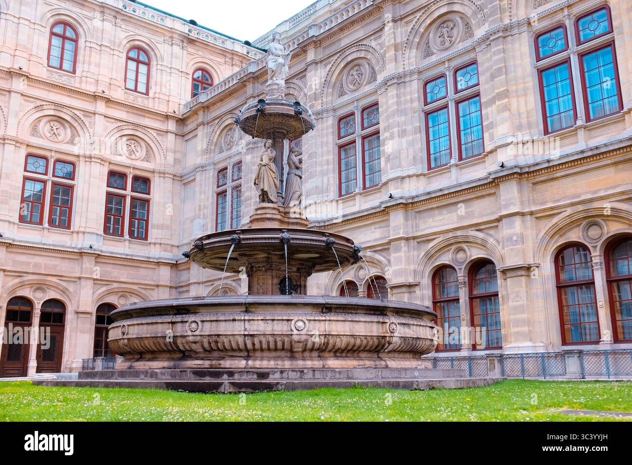 Fontana nel cortile dell'Opera di Vienna, circondata da ornate architetture rinascimentali e finestre storiche in un pomeriggio d'estate. Foto Stock