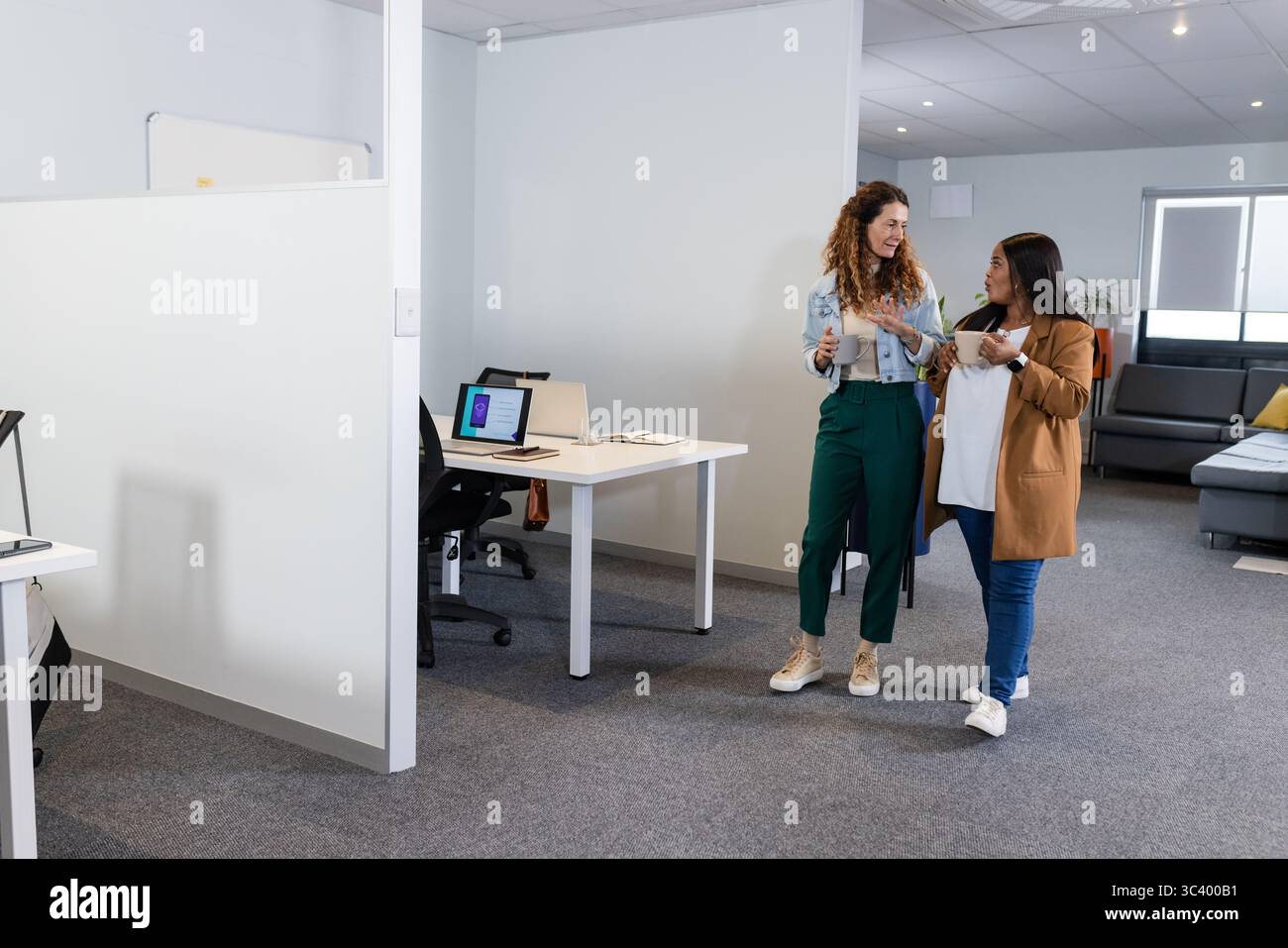 Diverse collaboratrici che camminano insieme in un ufficio open space tenendo tazze e spazio per copiare Foto Stock