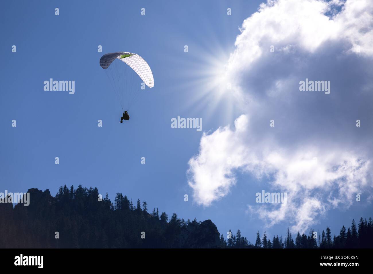 Un parapendio vola sotto un sole luminoso e nuvole nel cielo blu, Baviera, Germania Foto Stock