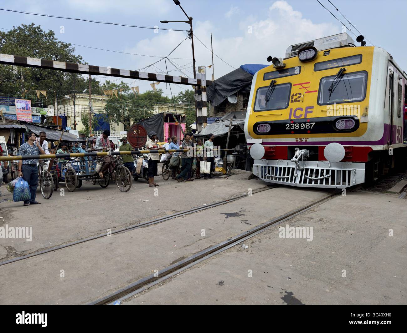 Treno pendolare che attraversa una strada con una folla in attesa, Kolkata, Bengala Occidentale, India Foto Stock