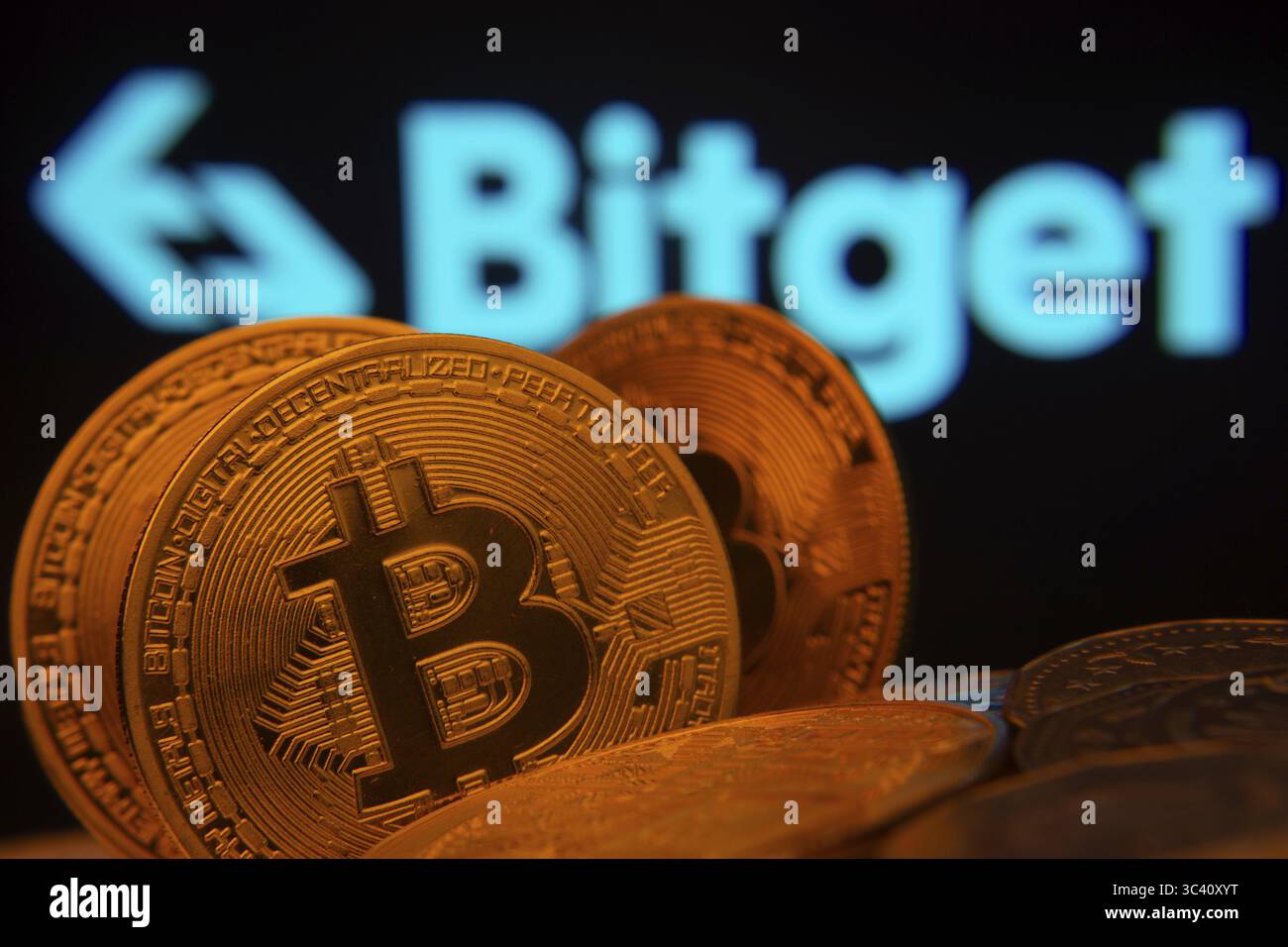 Dacca, Bangladesh- 27 luglio 2025: Primo piano delle monete Bitcoin con il logo Bitget visibile su uno schermo sullo sfondo Foto Stock