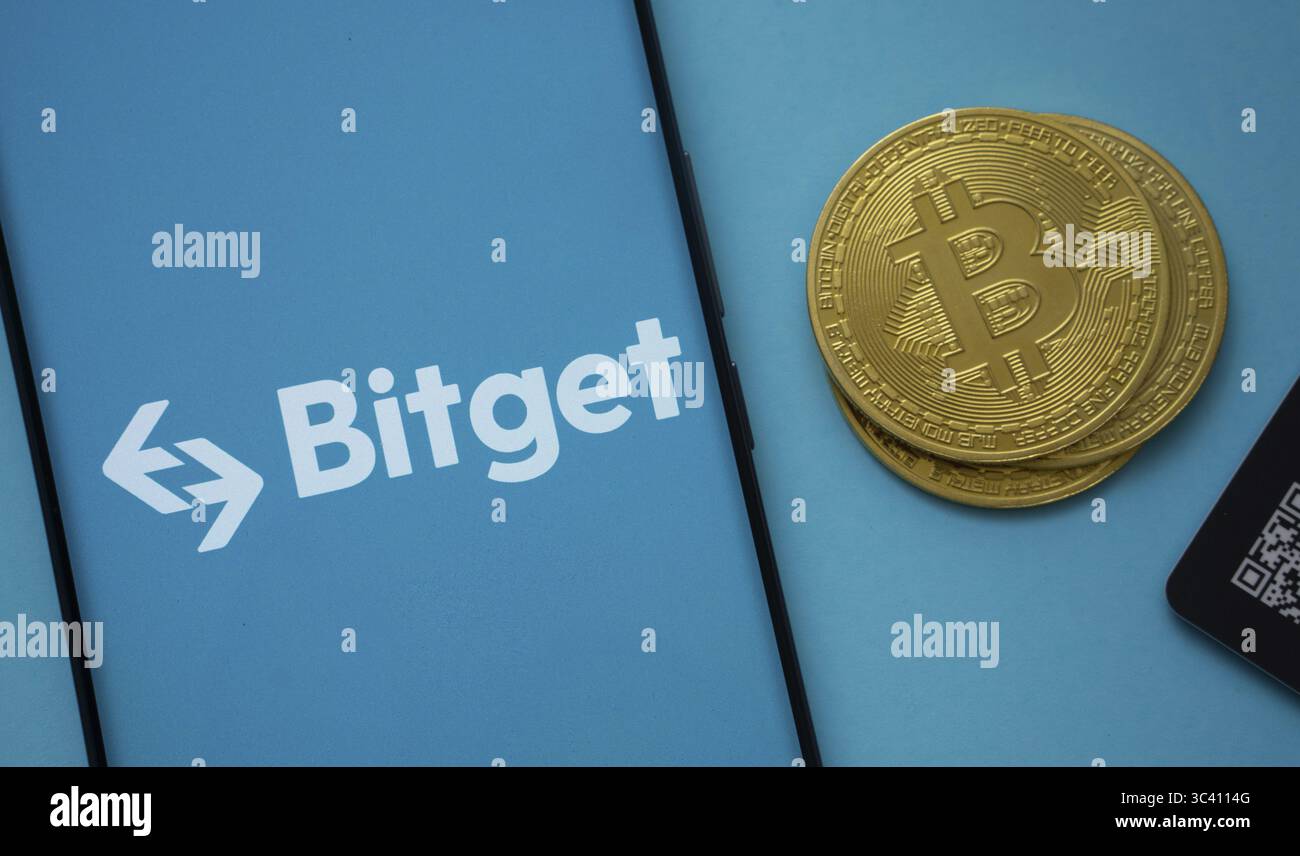 Dhaka, Bangladesh - 22 luglio 2025: Logo Bitget sullo schermo dello smartphone vicino alla moneta Bitcoin e codice QR su sfondo blu Foto Stock