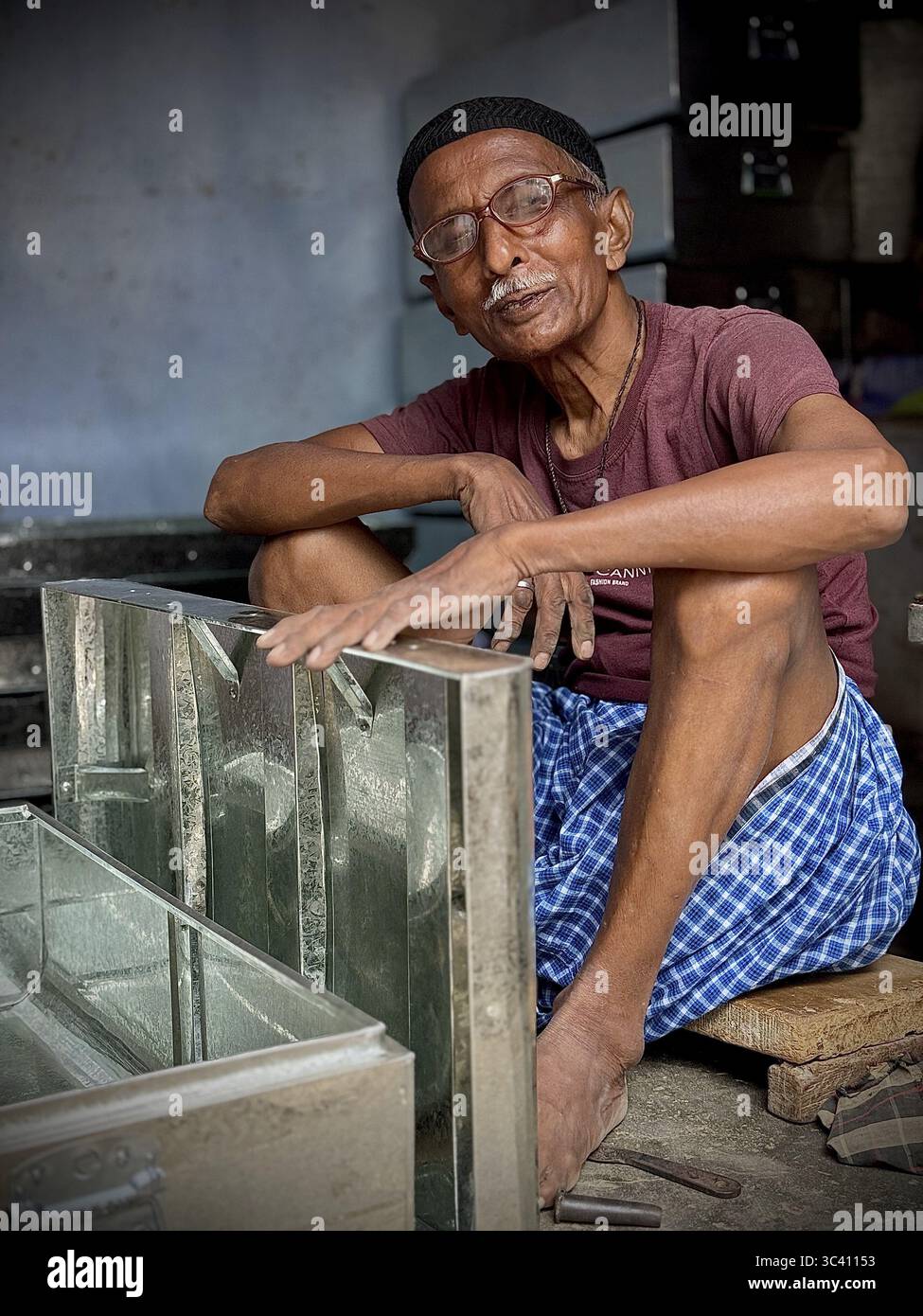 Uomo anziano che si concentra in un'officina, circondato da utensili metallici, Gaya, Bihar, India Foto Stock