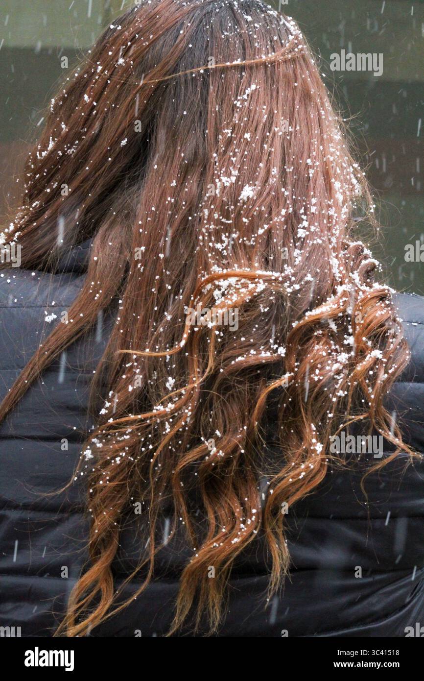 Neve che cade su lunghi capelli marroni ondulati visti da dietro Foto Stock