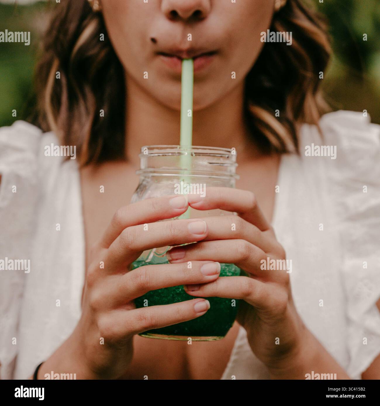 Donna che beve rinfrescante succo verde con paglia in estate Foto Stock