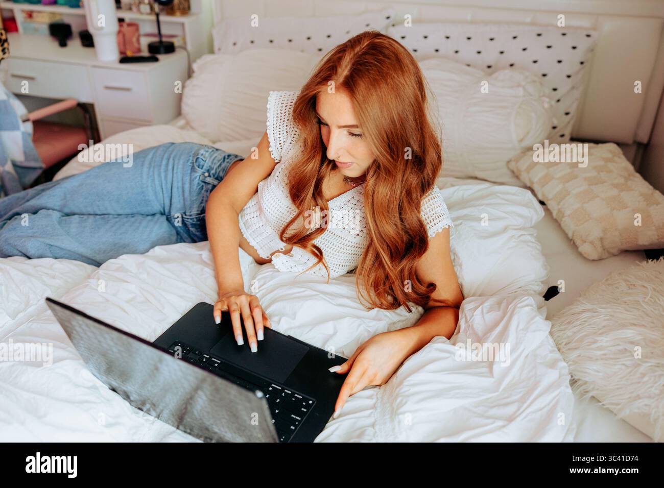 Donna rossa a letto che usa un computer portatile in una stanza luminosa Foto Stock