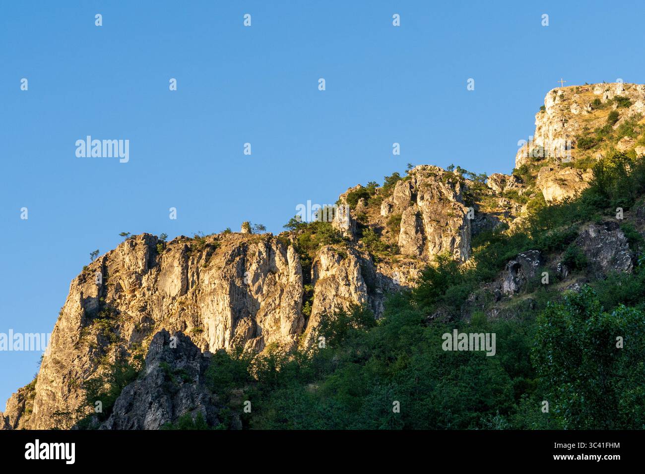 Scogliera baciata dal sole al tramonto: Luce calda contro cielo blu Foto Stock