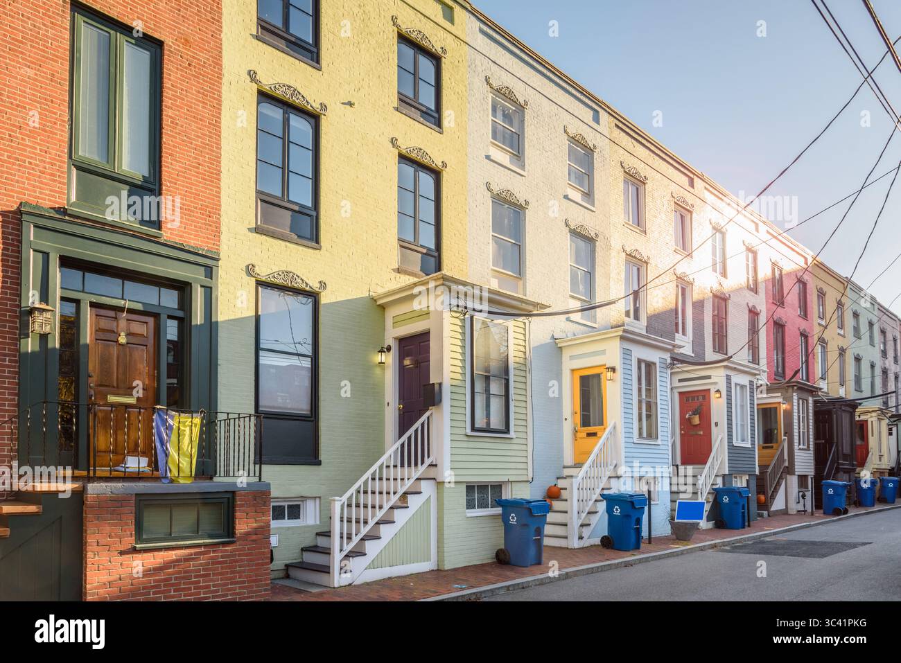 Vecchie case a file in mattoni color pastello con rampe di fili che conducono alle porte frontali in legno lungo una strada al tramonto in autunno Foto Stock