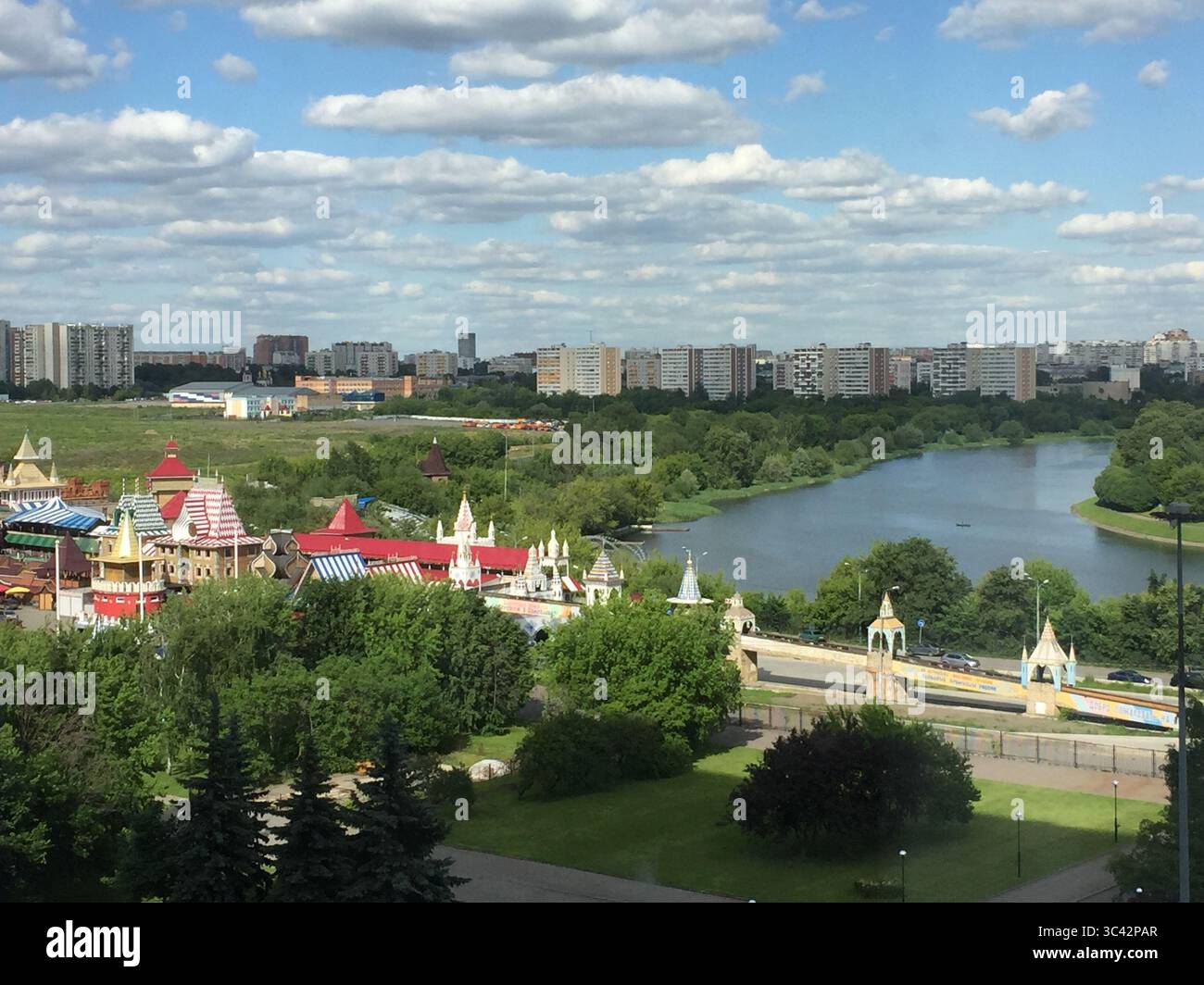Una vibrante vista aerea di un colorato parco divertimenti annidato da un fiume tranquillo, con il paesaggio urbano di Mosca, Russia, sotto un cielo parzialmente nuvoloso. Foto Stock