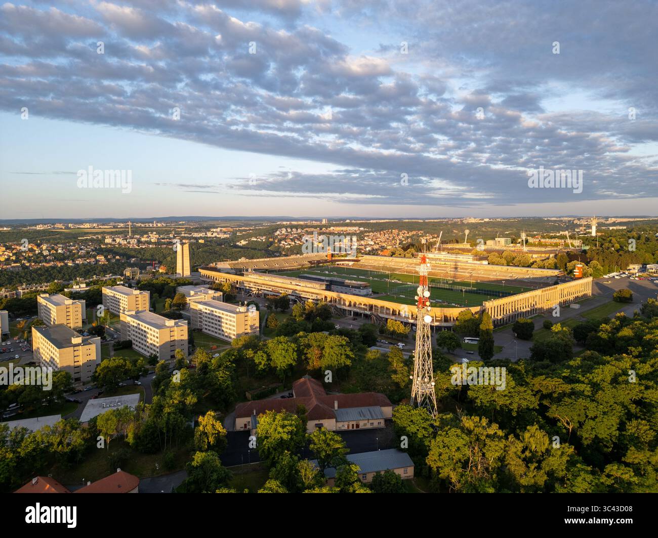 Il grande Stadio Strahov, circondato da una vegetazione lussureggiante, mostra la sua vastità durante il tramonto a Praga. Edifici e alberi creano un bellissimo paesaggio, mettendo in risalto la grandezza architettonica dello stadio. Foto Stock