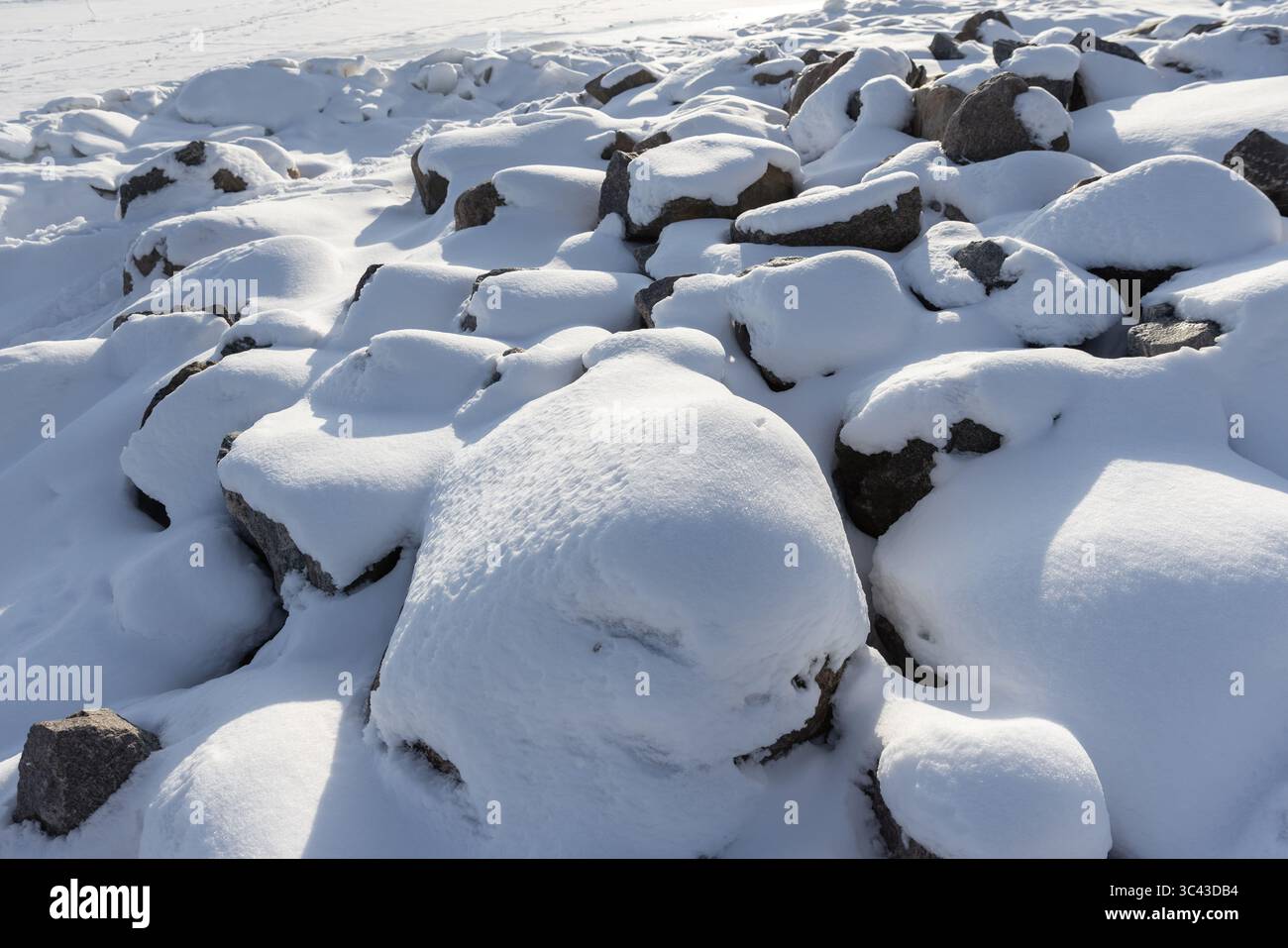 Una scena invernale frizzante che mostra rocce ricoperte di neve fresca, bagnate dalla luce del sole, creando un paesaggio naturale puro e sereno perfetto per la stagione Foto Stock