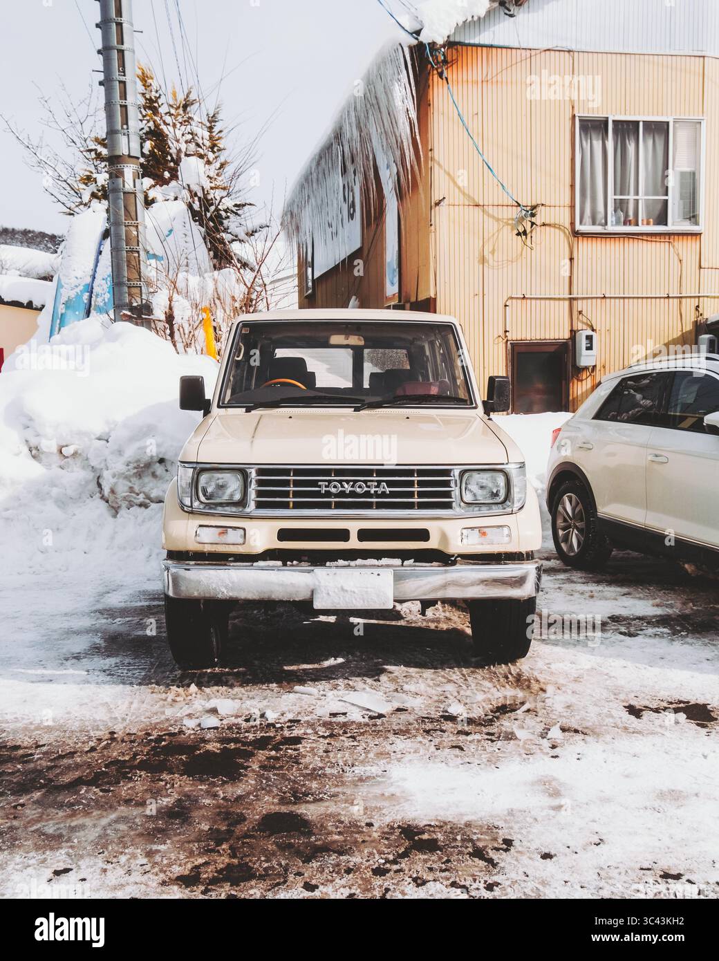 Lago Nojiri, Giappone - 23 febbraio 2025: Vista di un Toyota Land Cruiser d'epoca parcheggiato su un terreno innevato vicino a un edificio con ghiaccioli appesi al tetto. Foto Stock