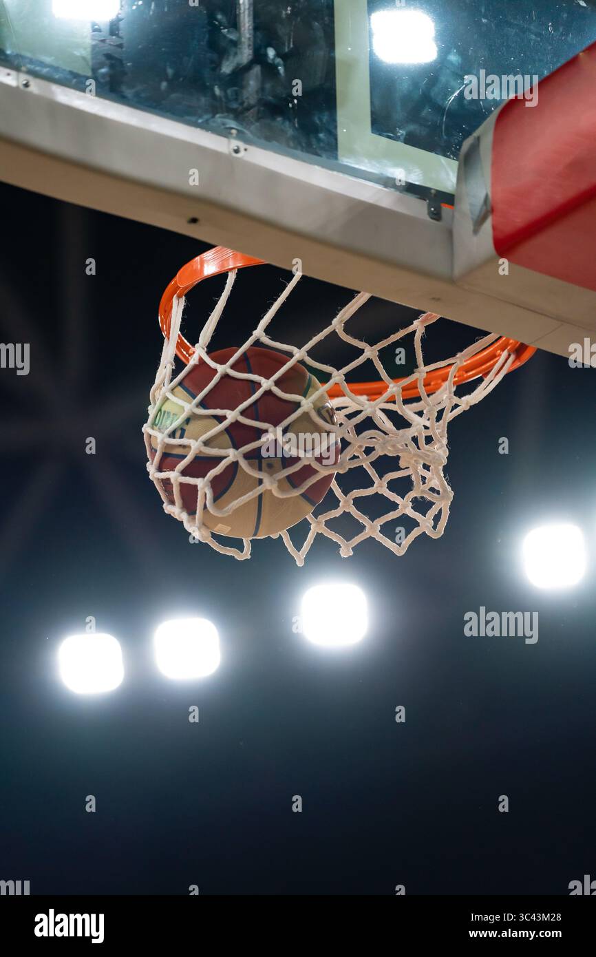 Pallacanestro che attraversa la rete durante una partita notturna, illuminata da luci luminose dell'arena, foto verticali, Stozice, Lubiana, Slovenia Foto Stock