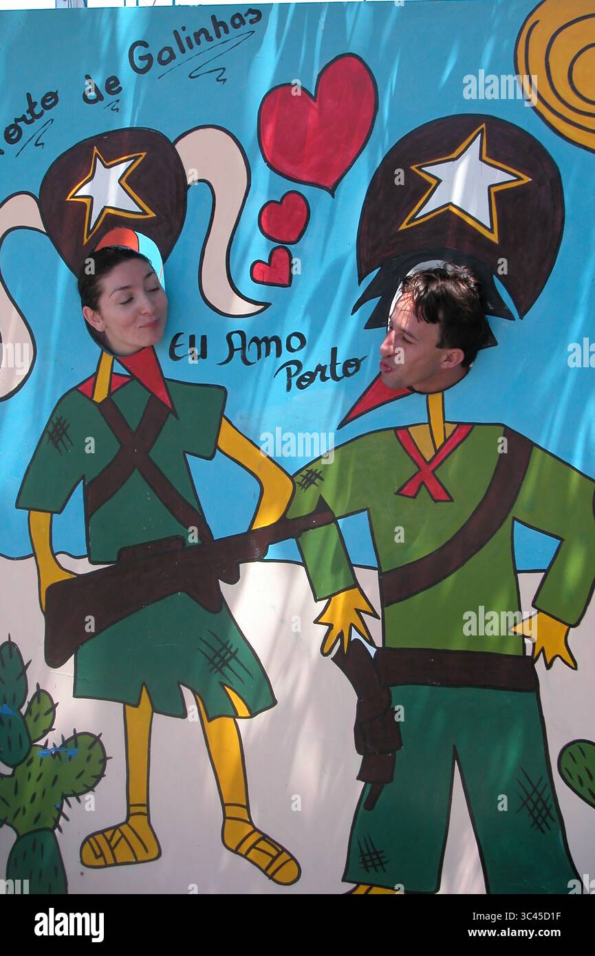 Un uomo e una donna posano per una foto con la testa attraverso una fessura su un tabellone dipinto. Il tabellone raffigura due soldati dei cartoni animati con le parole "EU amo Foto Stock