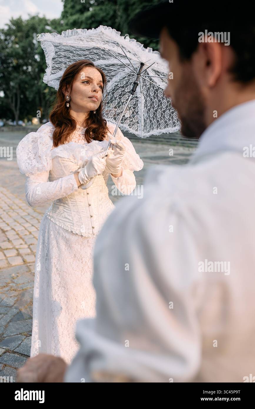 Donna in pizzo abito vintage con ombrello che guarda l'uomo fuori dalla cornice Foto Stock