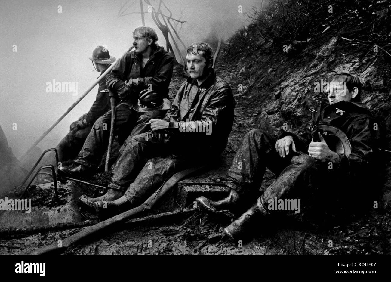 I vigili del fuoco a Burien, Washington, riposano dopo aver combattuto un incendio in casa. Questa fotografia ha vinto il Premio Pulitzer 1975 per Spot News Photography. Come riportato sul giornale: "Il fumo è appeso in aria mentre stanchi vigili del fuoco si sono riposati dopo un incendio di prima mattina che ha distrutto una casa di due piani sul lungomare Foto Stock
