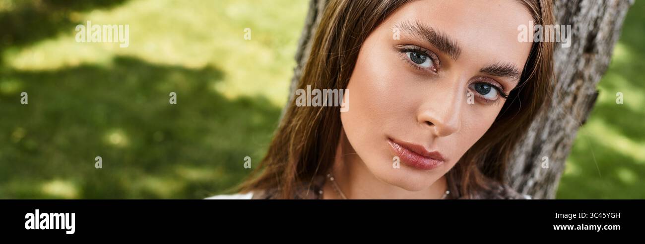 Una giovane donna si rilassa in un parco soleggiato e lussureggiante, perso nel pensiero. Foto Stock