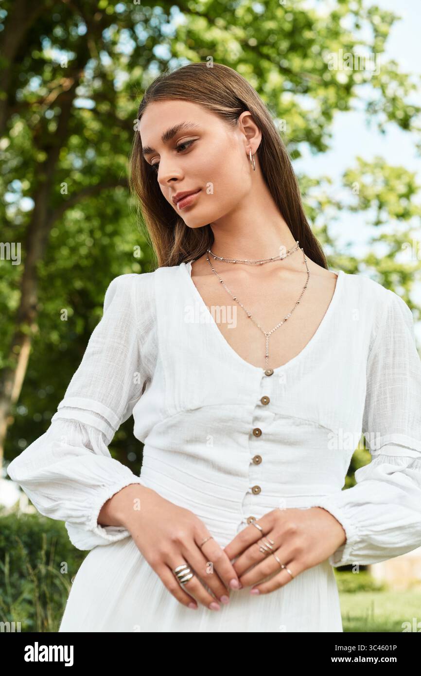 In un vivace parco verde, una giovane e bella donna irradia fiducia, vestita con un abito bianco. Foto Stock