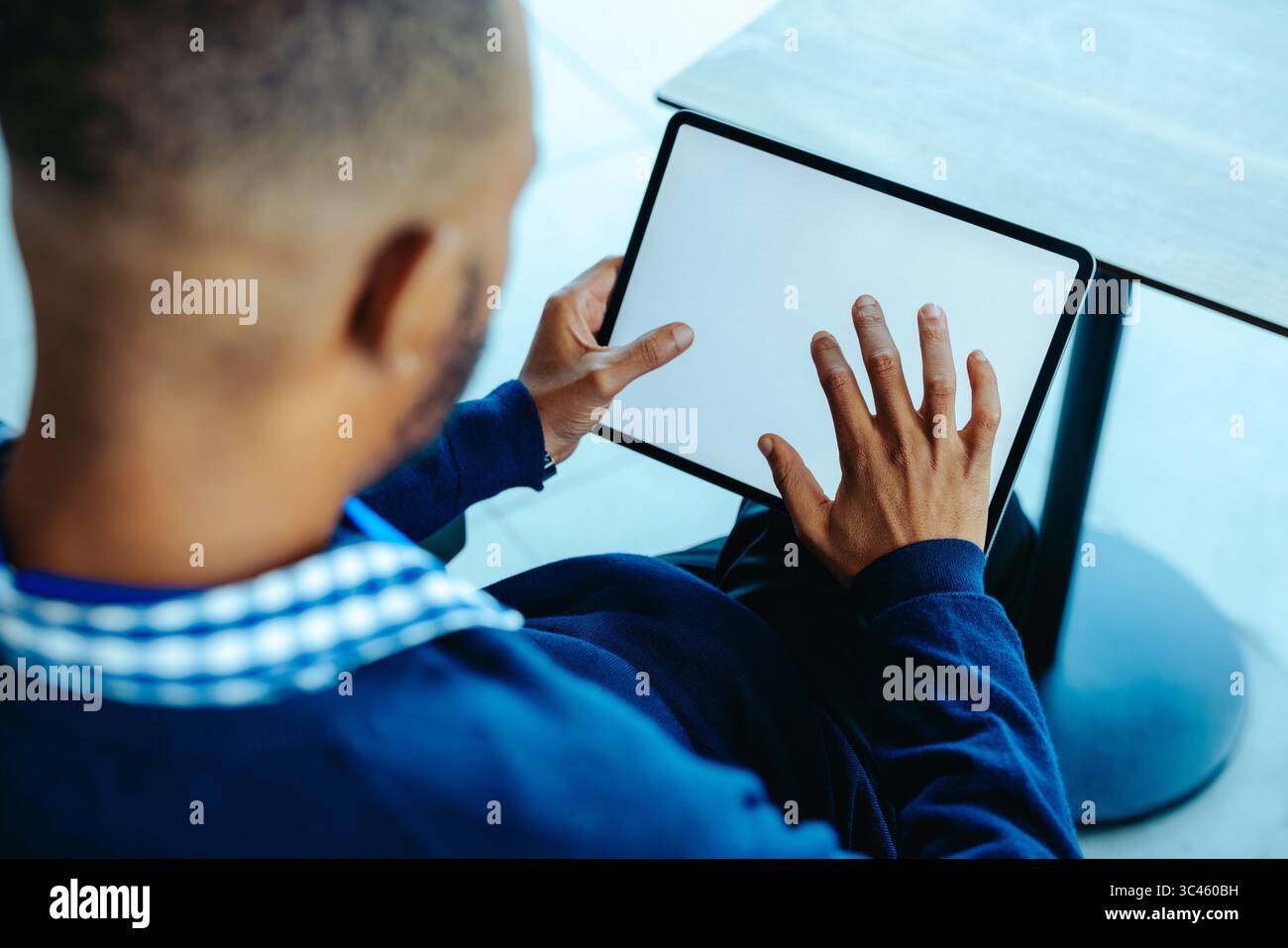 Un uomo d'affari ha un tablet vuoto, pronto a interagire con i contenuti digitali. Seduto a un tavolo elegante in un ufficio contemporaneo, è pronto per gli affari Foto Stock