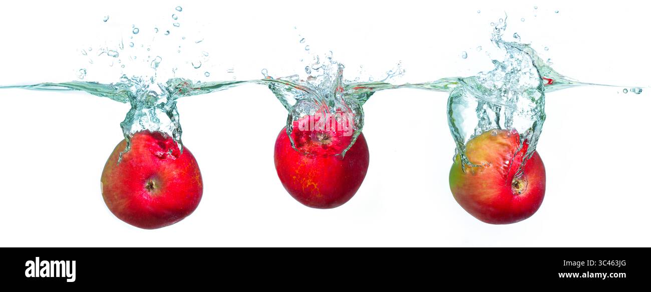 Gruppo di mele rosse brillanti che spruzzano in acqua limpida, creando bolle dinamiche e goccioline su uno sfondo bianco chiaro, evidenziando la freschezza Foto Stock
