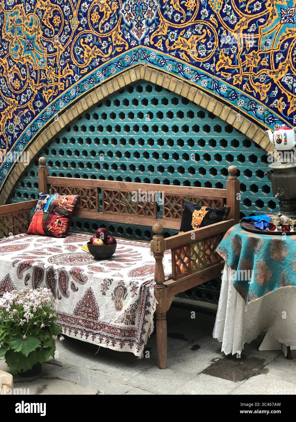Una tradizionale area salotto iraniana splendidamente decorata, caratterizzata da vibranti piastrelle islamiche, panca in legno con tessuti paisley Foto Stock