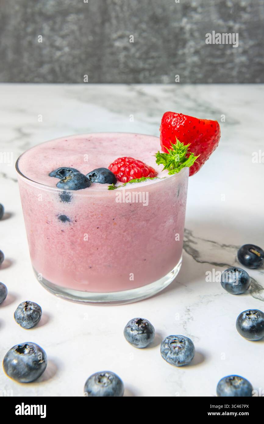 Frullato di mirtilli e cocco servito in un bicchiere, con uno sfondo rustico in legno e una luce soffusa del mattino Foto Stock