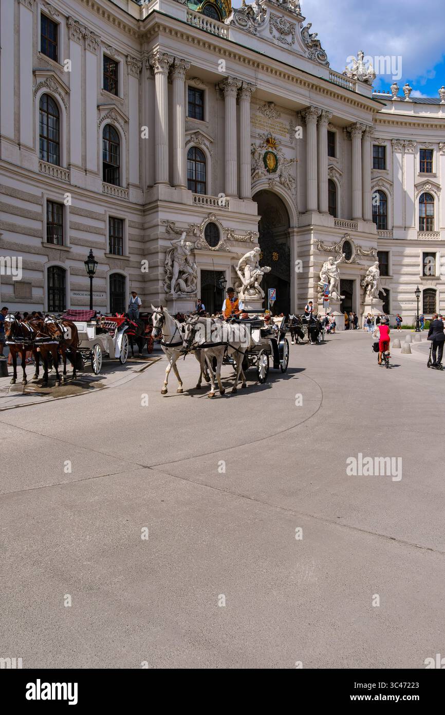 Scena quotidiana piena di turisti e carrozze trainate da cavalli su Michaelerplatz di fronte all'ala Michaelertrakt dell'Hofburg di Vienna, Vienna, Austria. Foto Stock