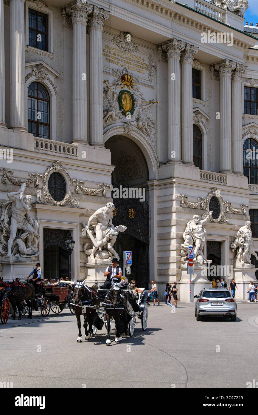 Scena quotidiana piena di turisti e carrozze trainate da cavalli su Michaelerplatz di fronte all'ala Michaelertrakt dell'Hofburg di Vienna, Vienna, Austria. Foto Stock