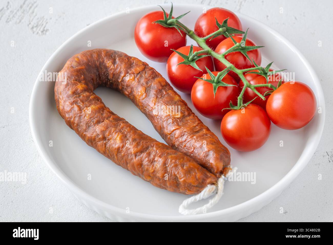 Una sola salsiccia e pomodori freschi posizionati semplicemente su uno sfondo luminoso e pulito Foto Stock