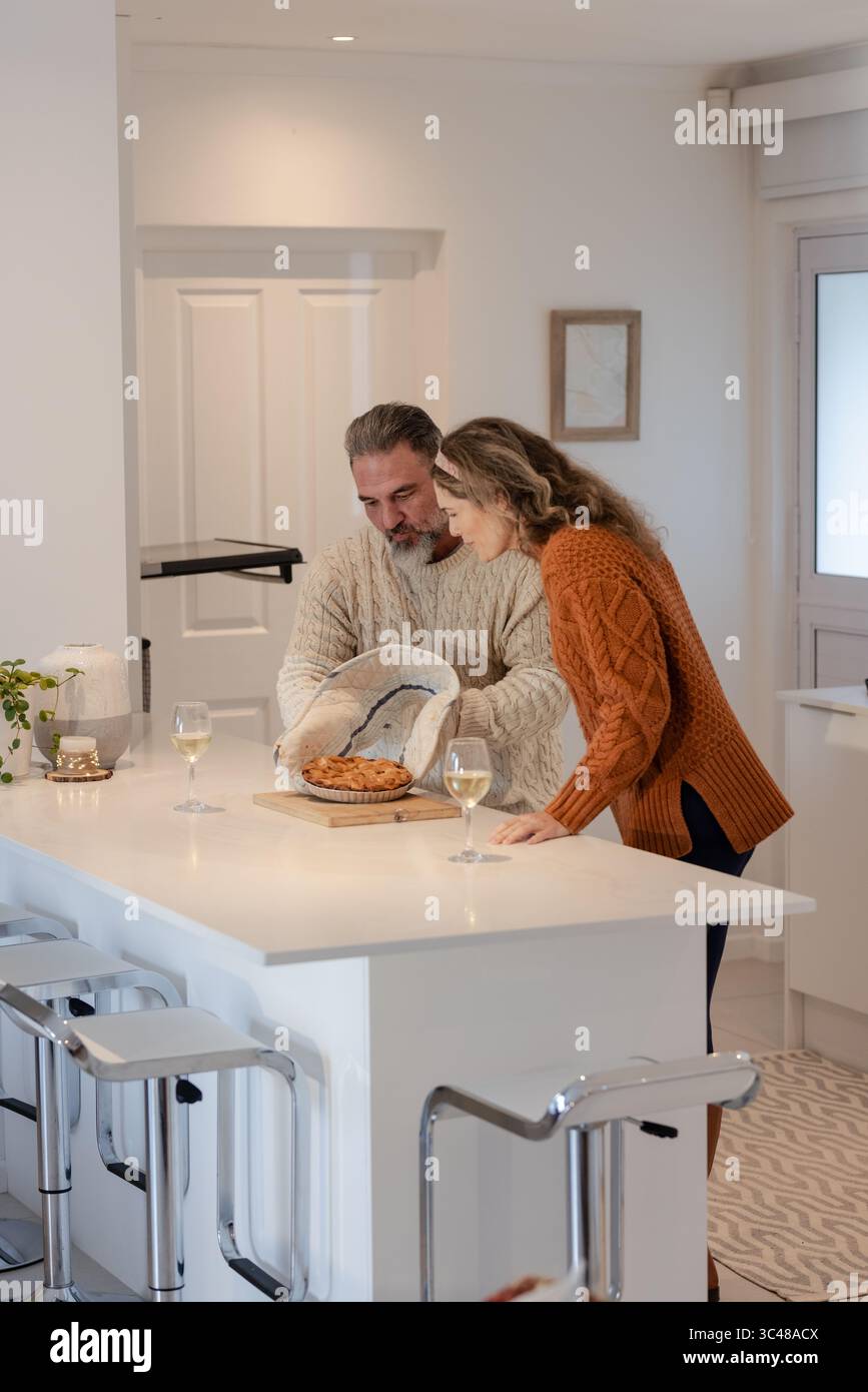 Coppia che solleva torta appena sfornata su un asse di legno usando un guanto da forno nella moderna isola della cucina Foto Stock
