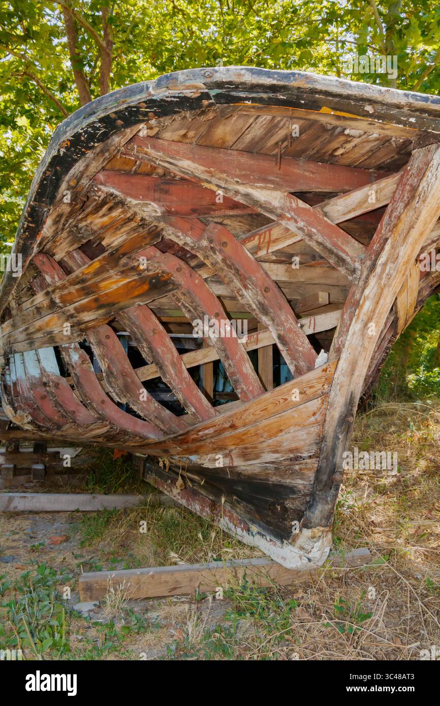 Una vecchia barca in legno con costole visibili e tavole decadute poggia su un terreno asciutto all'aperto, rivelando la sua struttura resistente agli agenti atmosferici e segni di abbandono o riposo Foto Stock