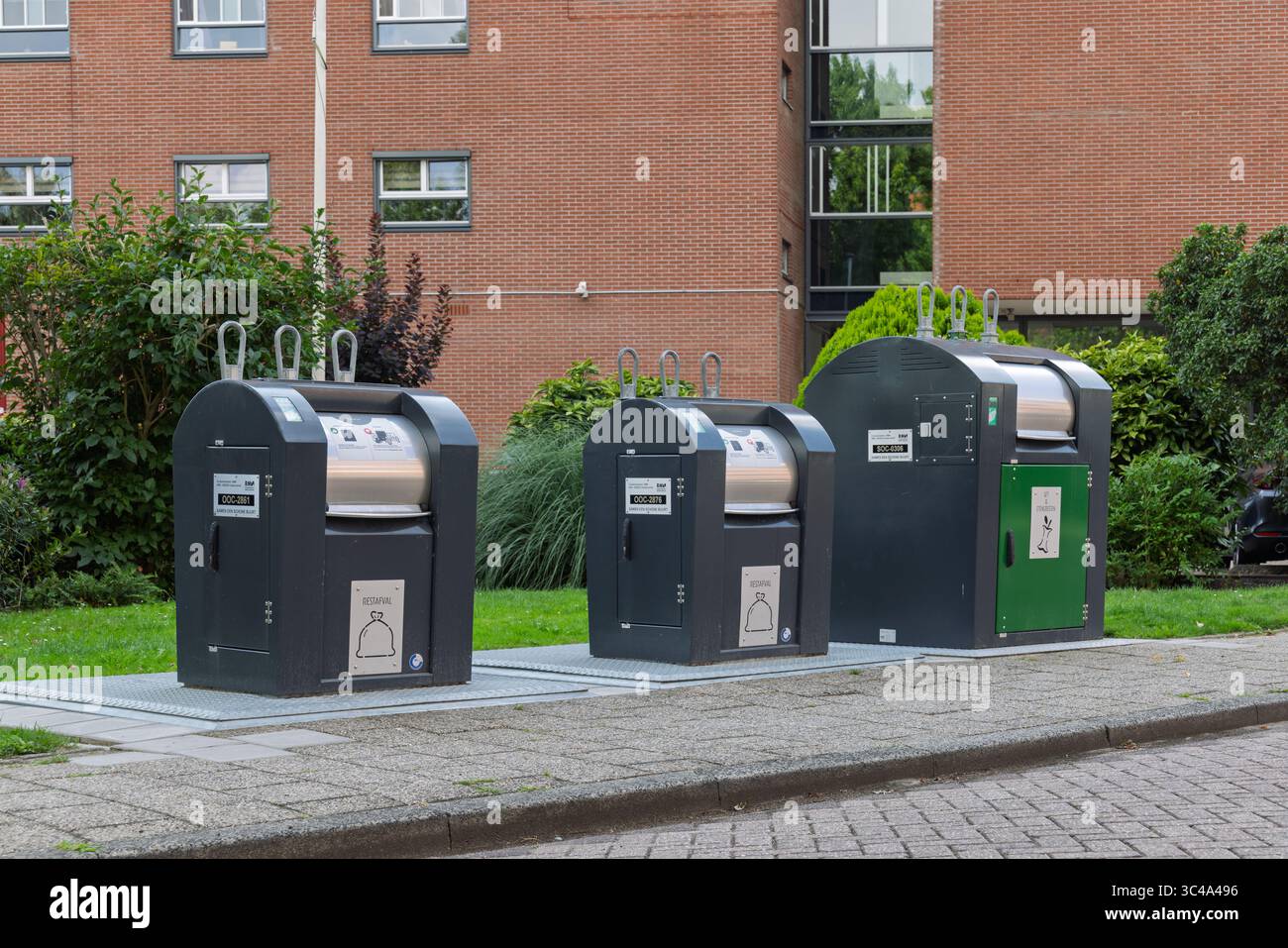 Tre moderni contenitori per rifiuti sotterranei, per diversi tipi di riciclaggio, sono allineati in modo ordinato su un'area pavimentata di fronte a un edificio in mattoni. Utrecht, Foto Stock