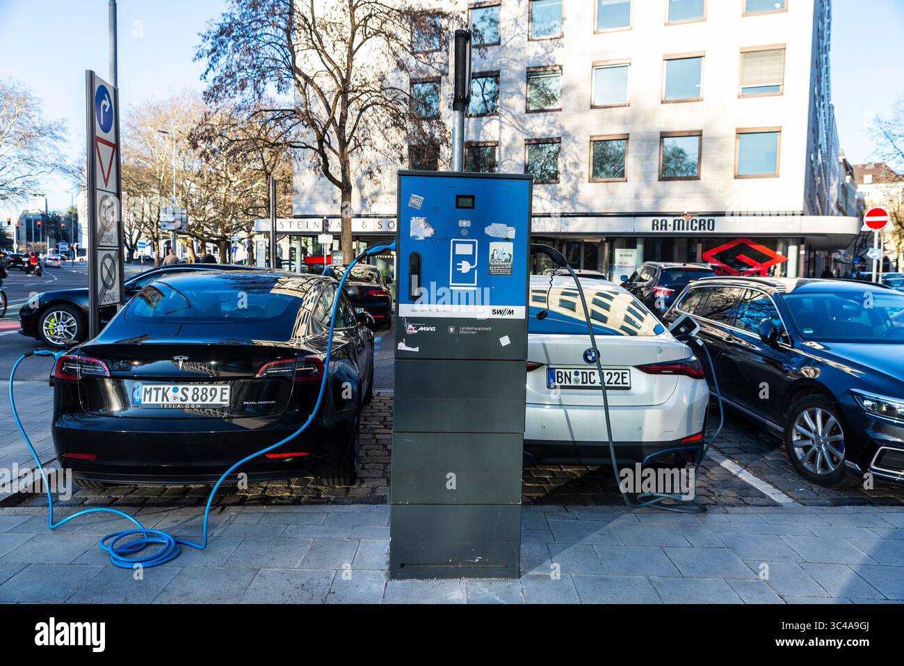 Monaco di Baviera, Germania - 4 aprile 2025: Auto elettriche, doppio motore Tesla e BMW i4, ricarica delle batterie in un punto di ricarica in una strada di Monaco, Germania Foto Stock