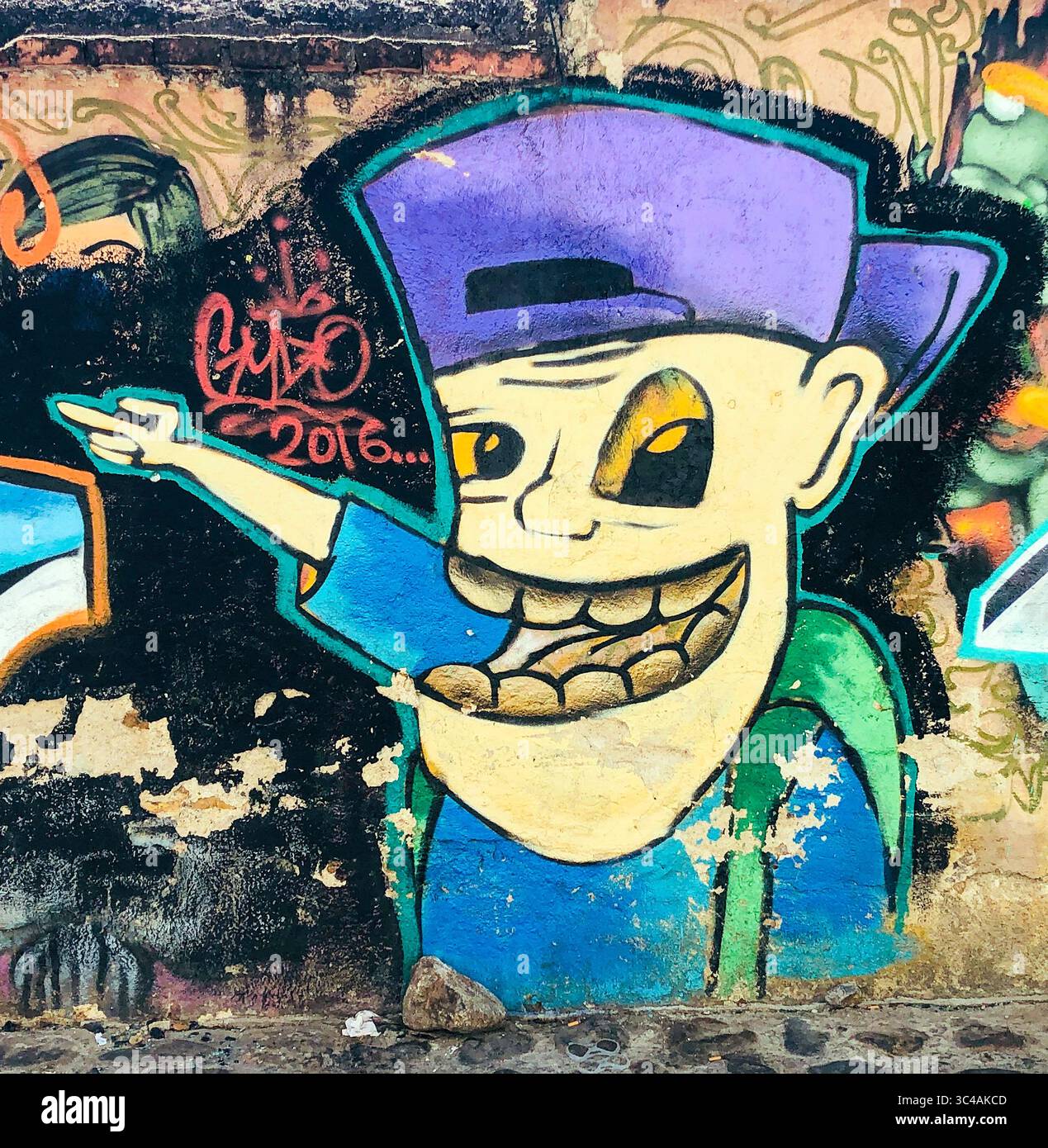 Il personaggio dei graffiti con un grandissimo sorriso e un cappello all'indietro illumina un muro di Oaxaca, in Messico, Street art con attitudine e stile locale. Foto Stock