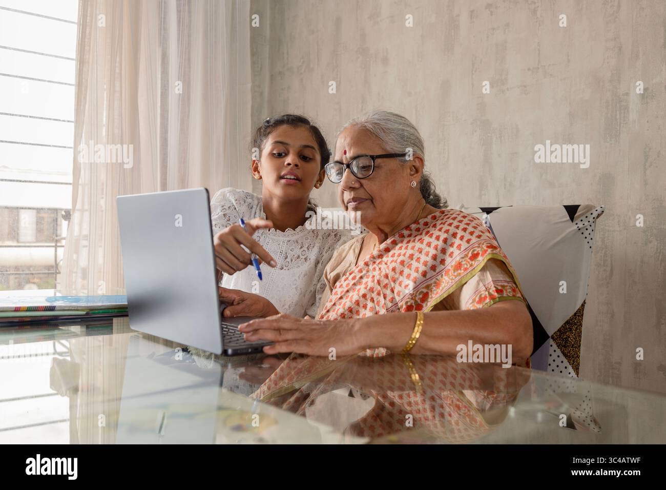 Nipote indiana che insegna alle donne anziane (nonna) a utilizzare il laptop a casa. Lavorare insieme per l'assegnazione scolastica utilizzando un laptop. Foto Stock