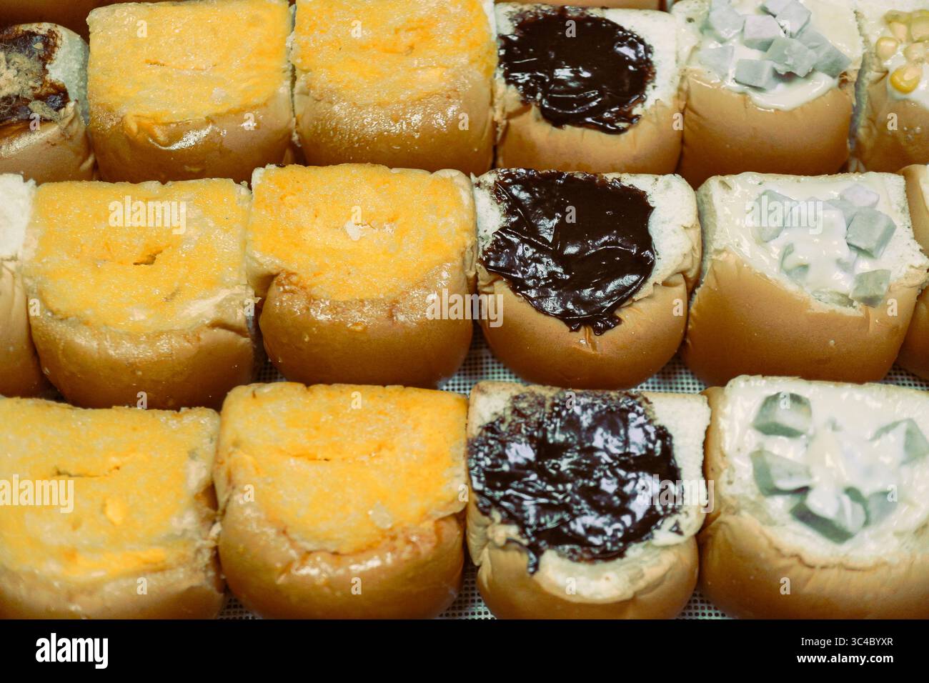 Panini tailandesi appena fatti ripieni di cioccolato, burro e crema taro, disposti ordinatamente in un vassoio Street food notturno con vapore caldo che sale. Foto Stock