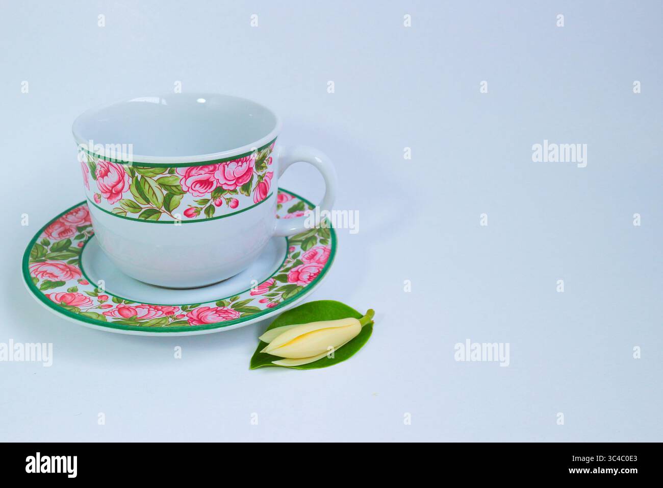 Tazza e piatto in ceramica vintage dal design rosa, accompagnati da fiori e foglie di champa freschi. Ripresa su sfondo bianco con spazio vuoto per il testo. Foto Stock